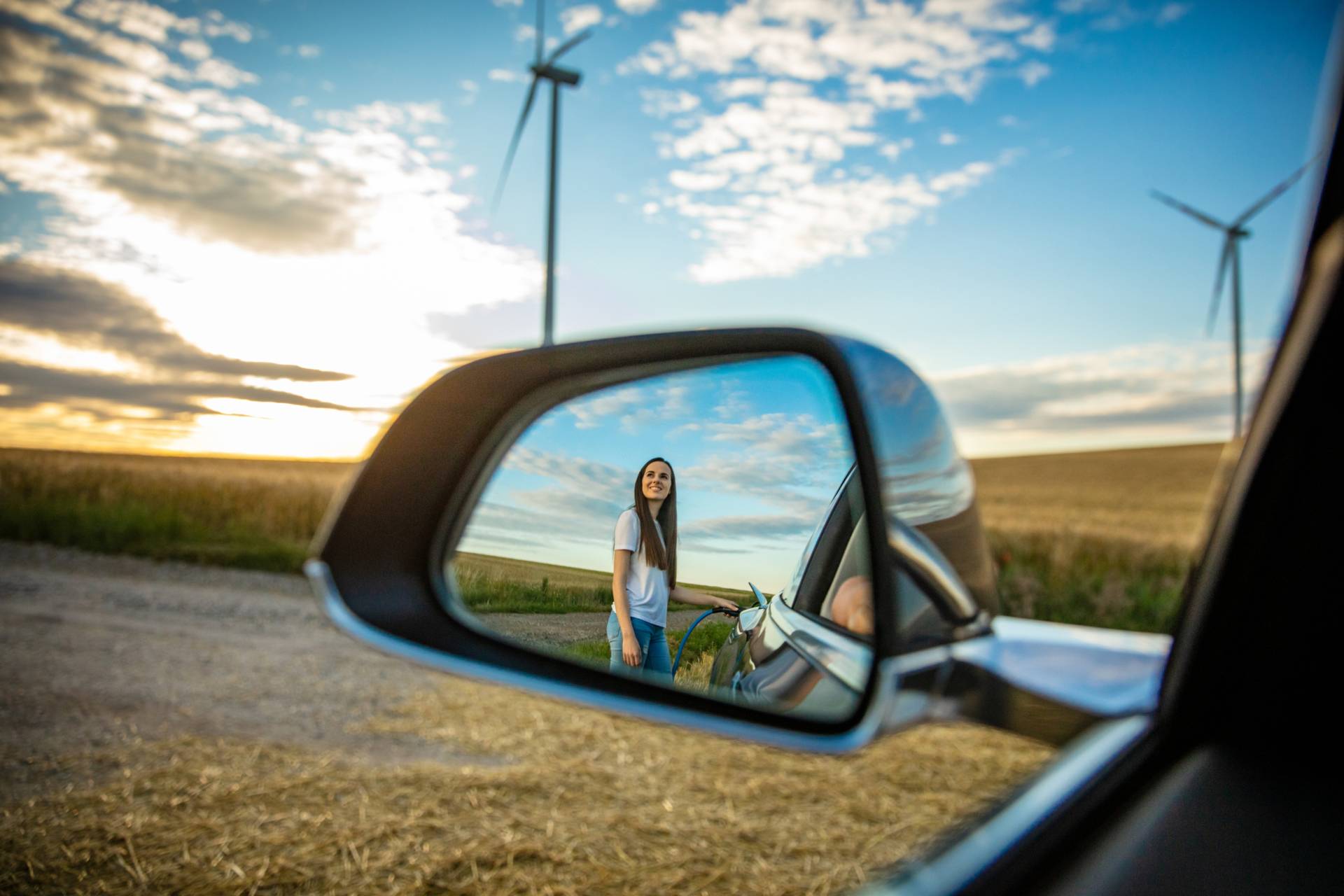 woman charging electric car staring at windmills