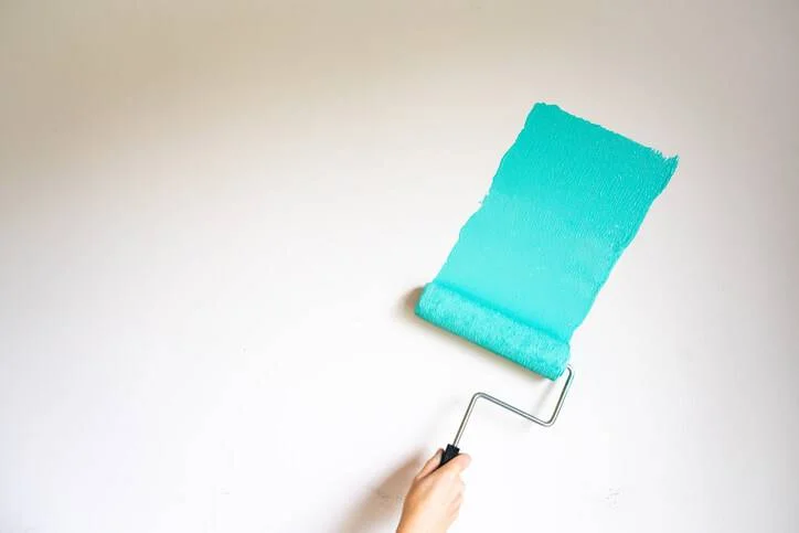 Paint roller applying teal paint to white all